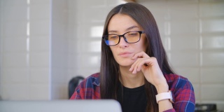 戴着眼镜的美丽白人女性在禁闭期间在家用笔记本电脑工作，思考着问题的解决方案。一个漂亮年轻女性在笔记本电脑前思考的4k视频