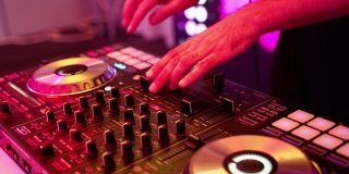 特写的DJ的双手扭动着，按下DJ遥控器上不同的按钮，颜色和轻音乐在俱乐部里。DJ派对。霓虹灯和运动的框架