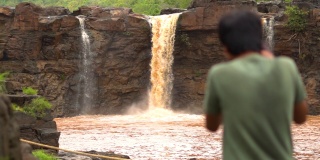 慢镜头拍摄的吉拉瀑布从一个小悬崖上落下，一个模糊的年轻的印度摄影师正在拍摄它。选择性地集中拍摄瀑布的游客。