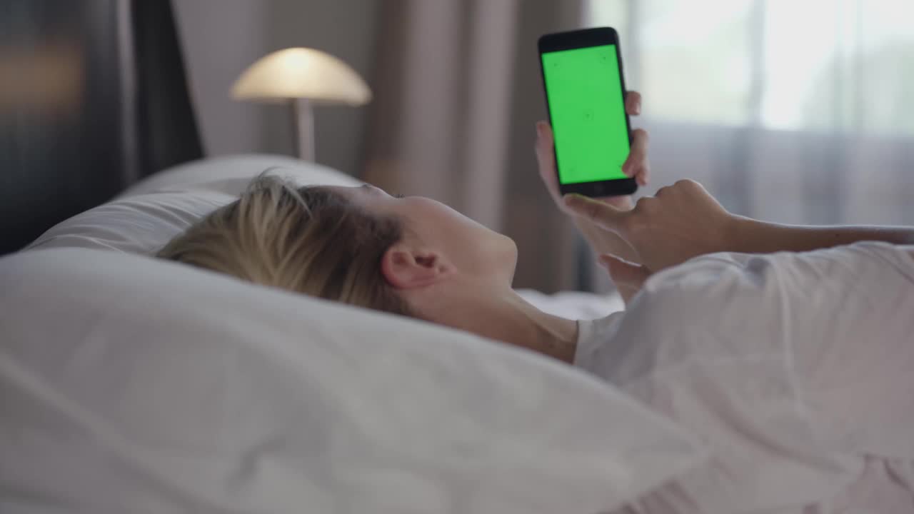 一个女人拿着一部绿色手机在床上闲逛。