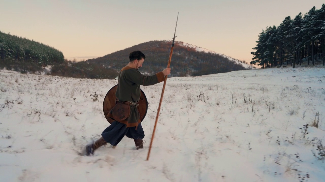 中世纪的武士手持盾牌和长矛，在夕阳西下的雪地上行走