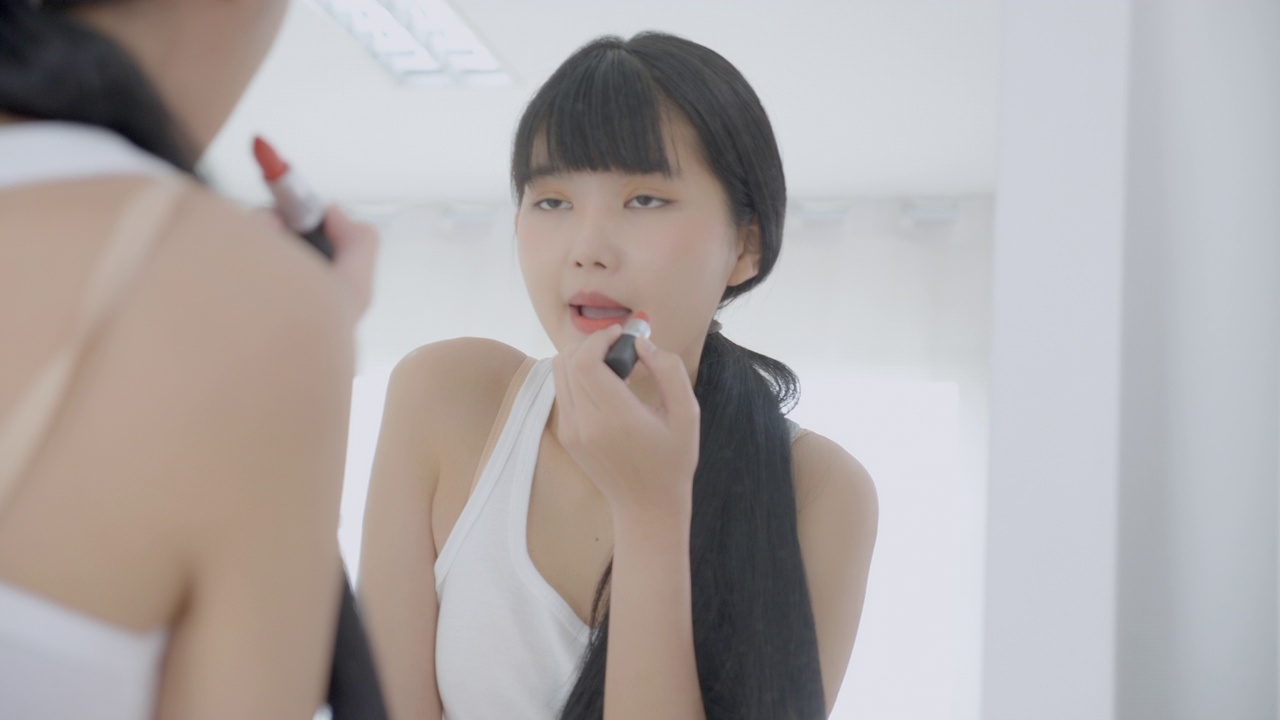 詳情圖-美麗年輕的亞洲女性涂口紅在嘴上，美麗的女孩看著鏡子的臉化妝化妝品與嘴唇的優(yōu)雅，化妝與性感的女性，皮膚護(hù)理和健康的理念。