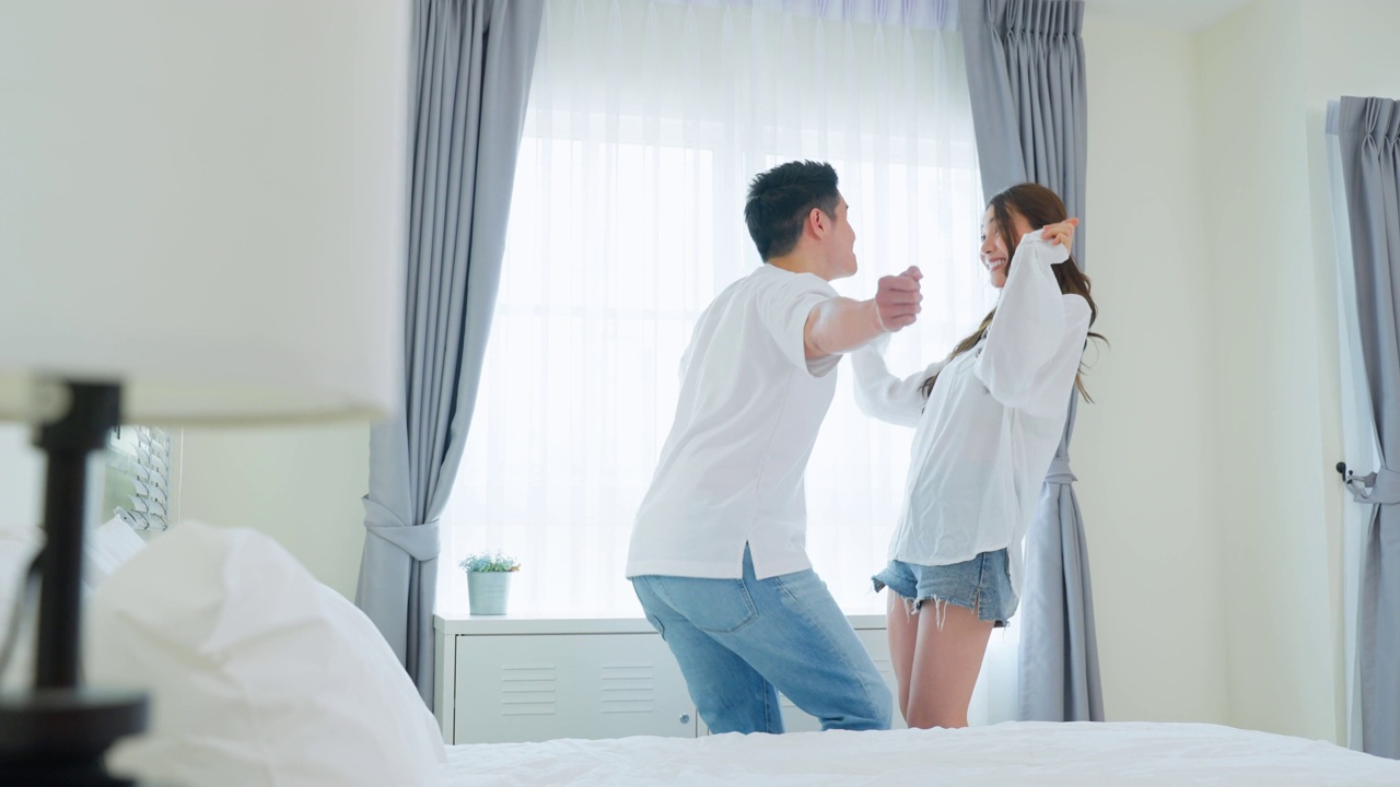 詳情圖-亞洲年輕情侶在家里的臥室里一起隨著音樂跳舞。迷人浪漫的新婚男女享受清晨醒來后在屋里花時間聽和唱歌