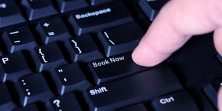 人类的手按下了电脑键盘上的Book Now按钮的特写