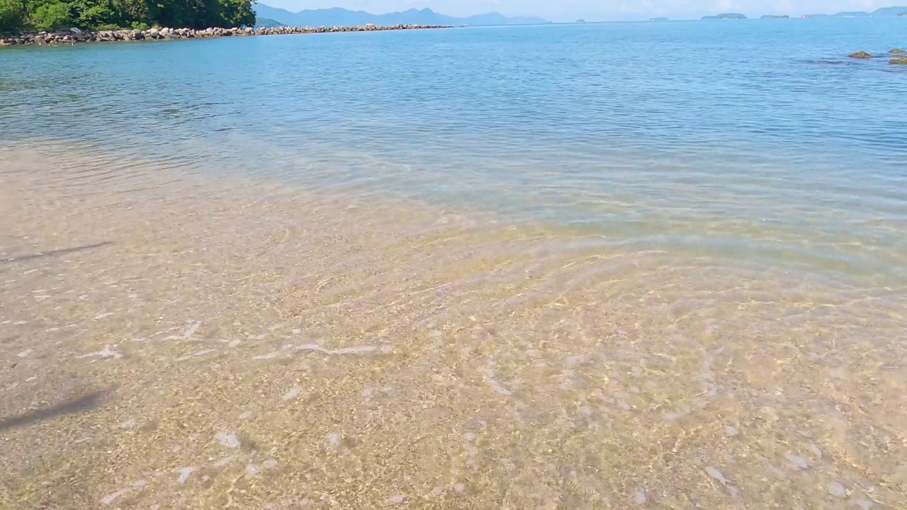 在阳光明媚的日子里，沙滩上的沙子被海浪拍打着。以石头屏障为背景的海滩。热带海滩，美丽的海滩，海浪