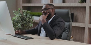 长相英俊的非裔美国人办公室职员在电脑屏幕前显得很高兴和满意。积极的反馈，很棒的结果，欣赏