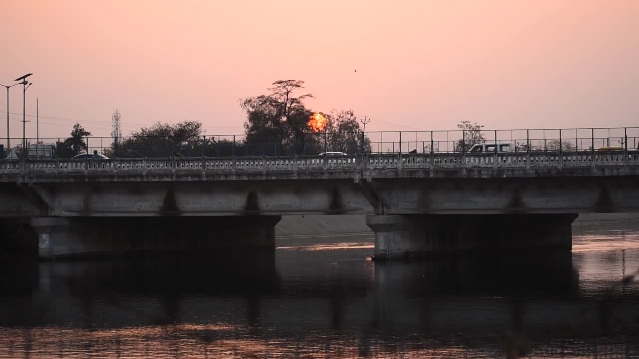 印度古吉拉特邦甘地那格的纳尔默达运河大桥的剪影。过桥车辆。桥在河水中的倒影，鸟儿在夜晚的天空中飞翔