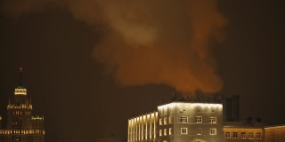 夜晚的城市里，浓重的蒸汽笼罩着建筑物。街道上的老式酒店灯火通明。外部装饰。冬季假期。4 k的片段