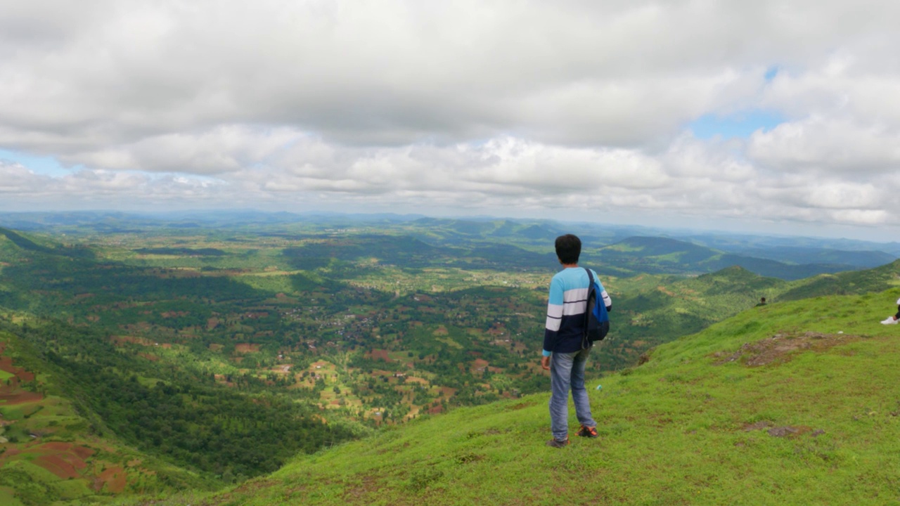印度男性徒步旅行者看着美丽的绿色葱郁的山谷，从萨普塔拉萨哈德里山脉的总督山山顶在古吉拉特邦，印度。徒步旅行者从山上欣赏风景。