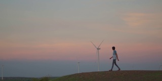 日落时分，印度古吉拉特邦万卡纳，一名印度男子走在风电场的风车前。环境可持续性的背景。希望绿色能源取代化石燃料。
