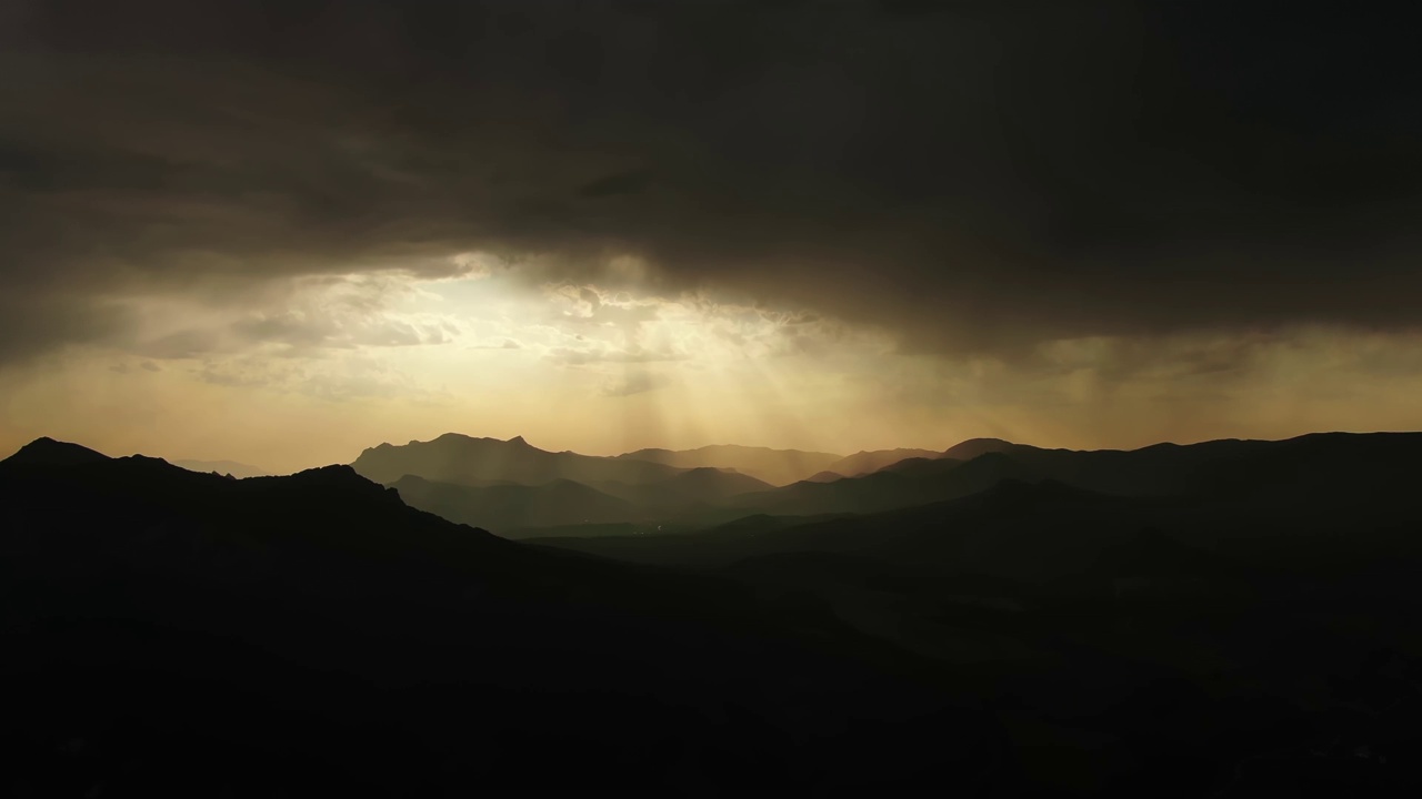 雷暴前的自然山脉全景，令人赏心悦目。从乌云中透出来的明亮阳光照亮了岩石山脉的轮廓