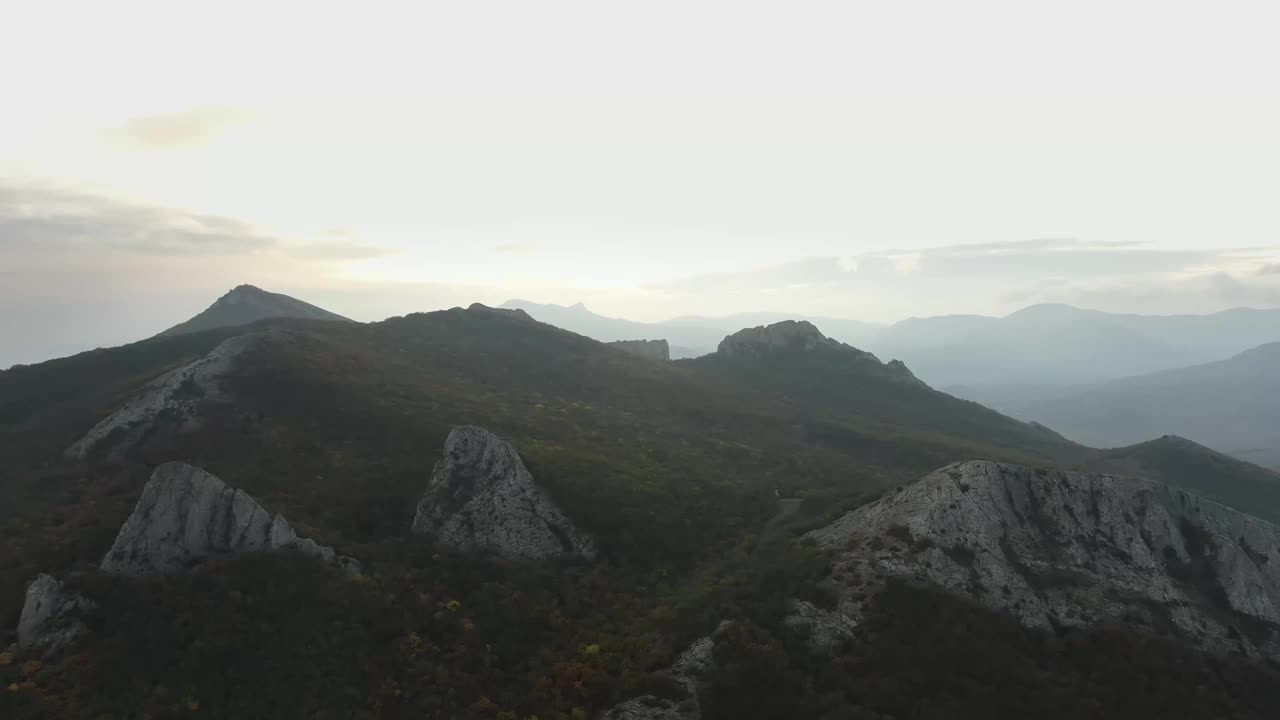 航拍慢镜头拍摄的是被秋天的森林和地平线上的日落覆盖的岩石山脉。舒缓的镜头与山的全景