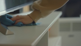 一位年轻女子用一块蓝色的抹布在电视机旁擦灰尘。打扫屋子。女主人的家务职责一只手的特写。景深