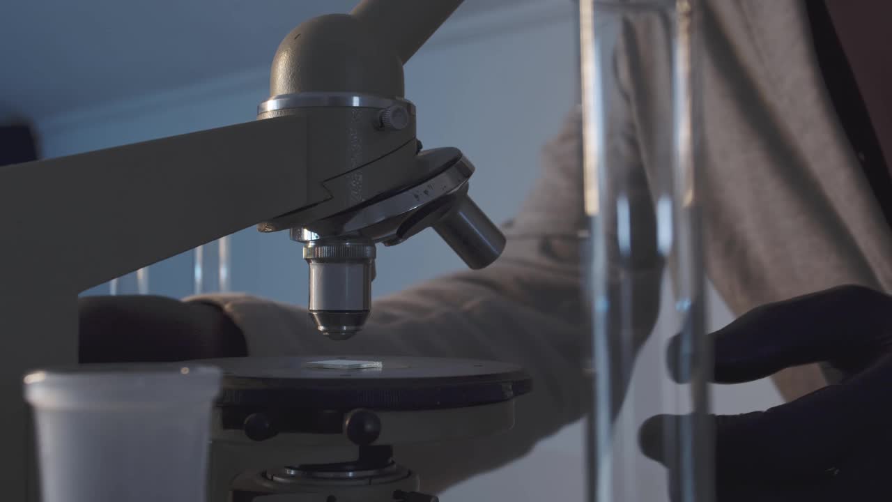 一个人在实验室里把显微镜放在玻片上的特写。在科学实验室工作。学校科学项目。人手戴橡胶保护手套。