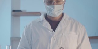 医生穿着晨衣，戴着防护橡胶手套，戴着护目镜，在近距离观察瓶中的液体是否有异味。科学实验室的研究工作。