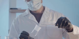 科学实验室的研究工作。一名医生穿着晨衣，戴着防护橡胶手套，戴着眼镜，近距离检查了烧瓶里的液体。