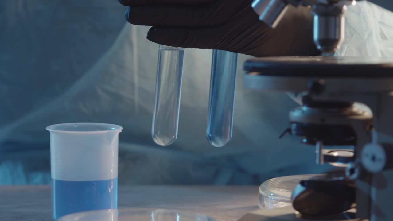一名戴着防护橡胶手套的实验室助理将两种液体与移液管在他手中的烧瓶中混合。以实验室设备为背景。