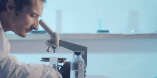 一位男性研究人员看着显微镜的目镜，调整其焦距。科学实验室的研究工作。实验室背景以蓝色区域突出显示。