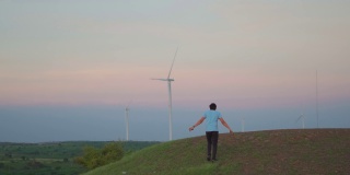 日落时分，印度古吉拉特邦万卡纳，一名印度男子在风电场的风车前爬上小山。环境可持续性的背景。希望绿色能源取代化石燃料。