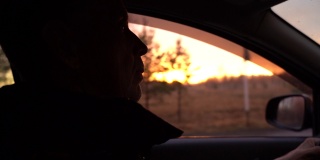 一个成年男子在夕阳的映衬下开车。