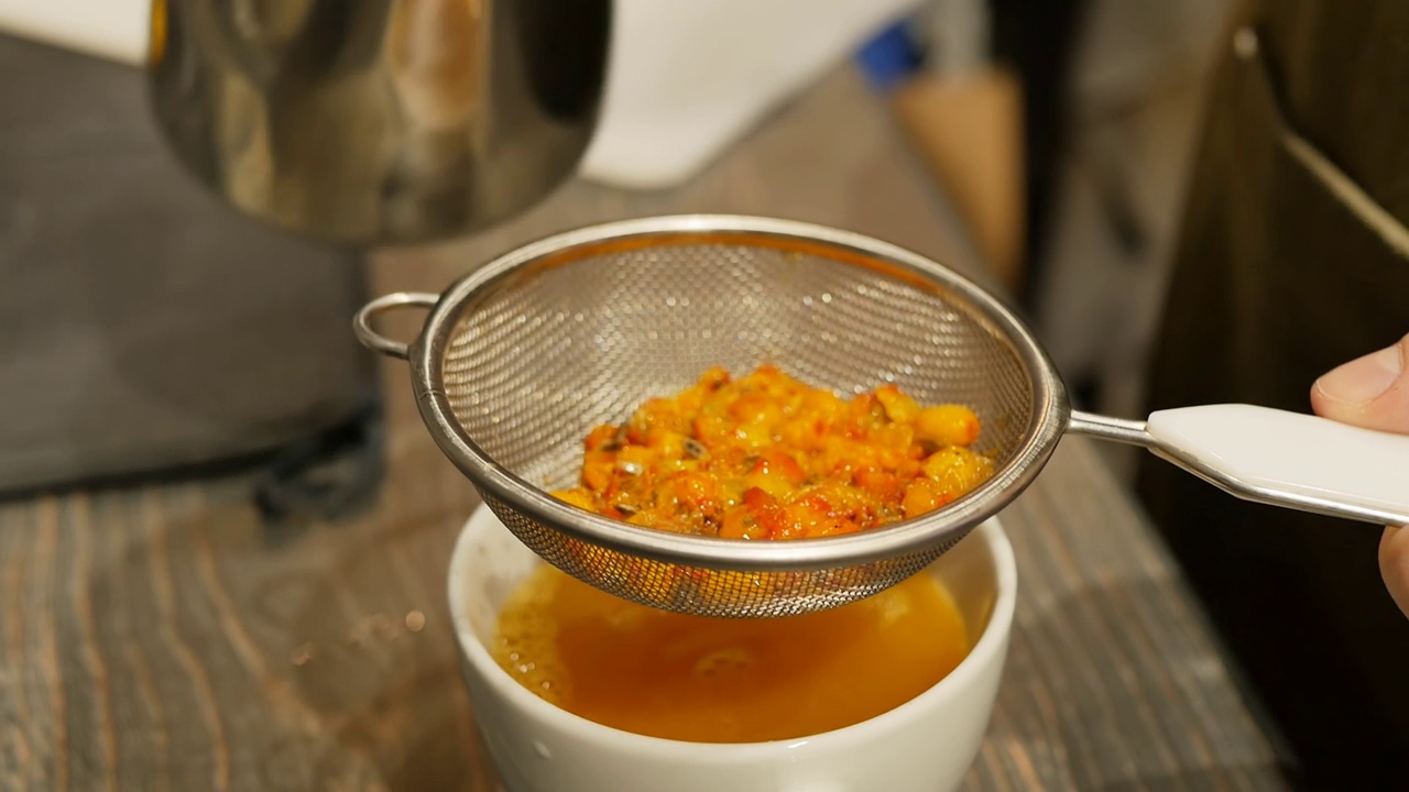 手用筛子把沙棘饮料过滤到杯子里