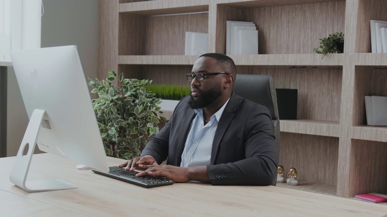非洲裔美国男性商人在办公室工作期间使用电脑打字。成年的公司老板坐在办公桌前。现代成功人士的概念。商业领导与管理理念