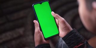 近距离的年轻人手使用智能手机与绿色屏幕