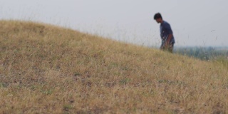 草地的特写镜头，一个模糊的人在背景中行走。夏季旅行背景。有选择地集中在那个印度人前面的草地上。