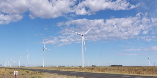 风力发电场建在路边的田地里。风车缓缓转动，蓝天飘着朵朵白云