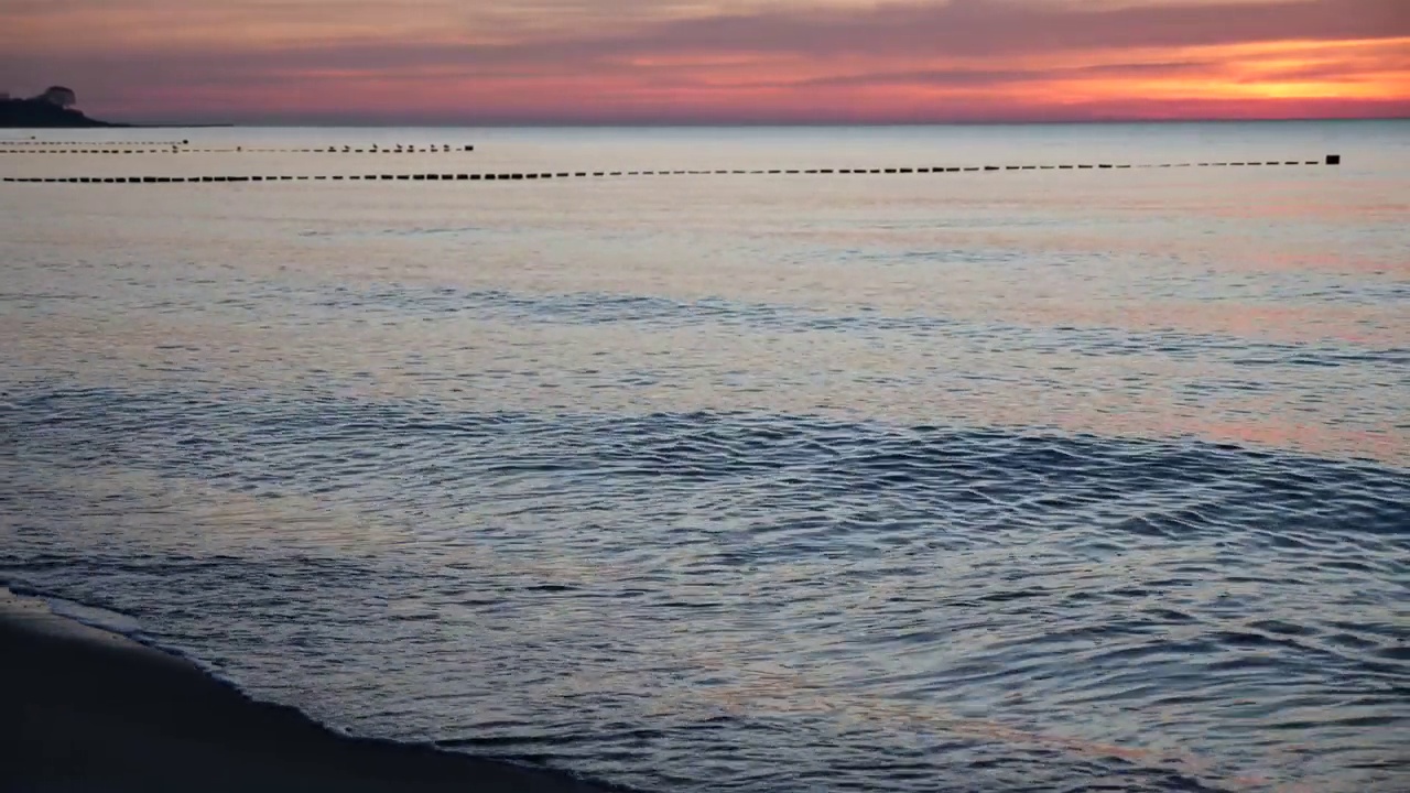 波罗的海西岸，夕阳西下，天空泛红，沙滩上的波浪