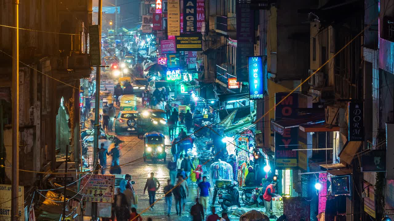 时间推移的主要集市街道显示霓虹灯招牌，商店，交通和行人在夜间在德里中心，印度，缩小