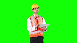 男性工程师穿着安全背心和头盔，在绿色屏幕背景前使用数字平板电脑工作