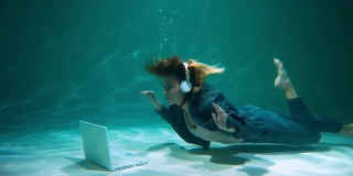 年轻美丽的商业女性潜水水下使用笔记本电脑网络摄像头视频呼叫慢动作。
