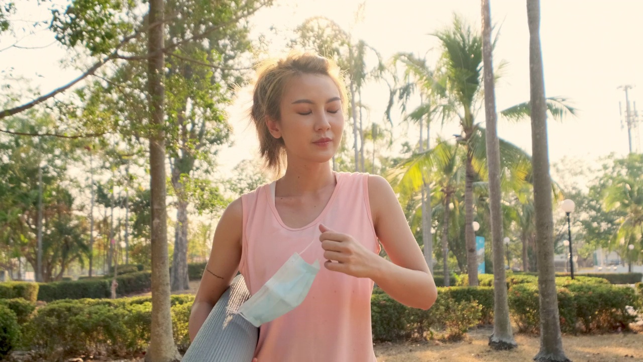 詳情圖-新常態(tài)健康生活理念。一名年輕的亞洲女性從COVID-19疫情中康復(fù)后，摘下醫(yī)用口罩，在公園室外練習(xí)瑜伽。