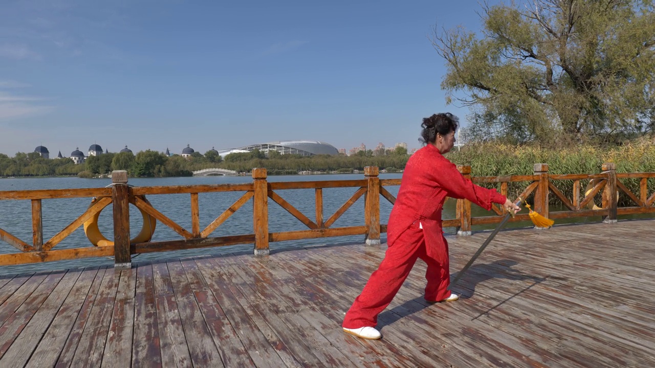 一位女士在湖边练太极剑。