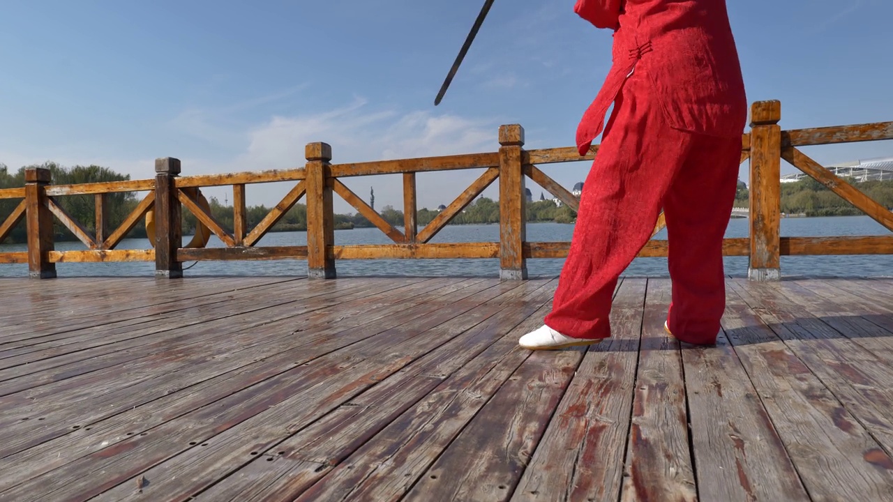 一位女士在湖边练太极剑。
