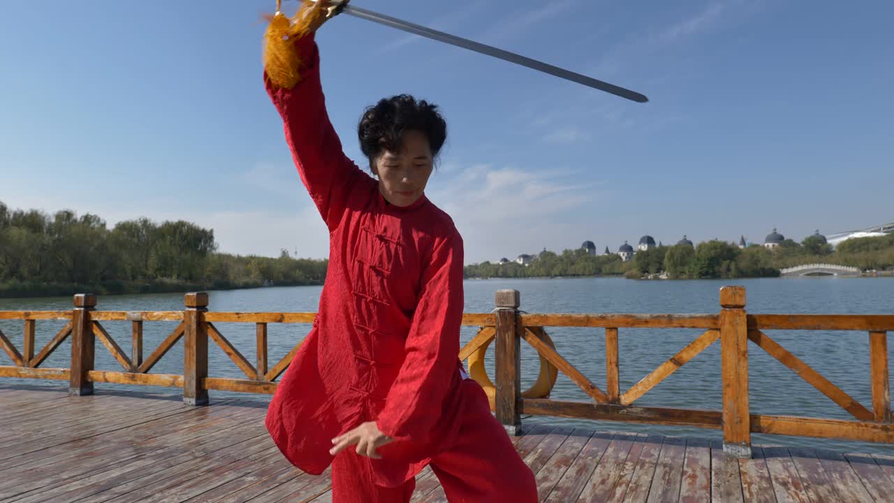 一位女士在湖边练太极剑。