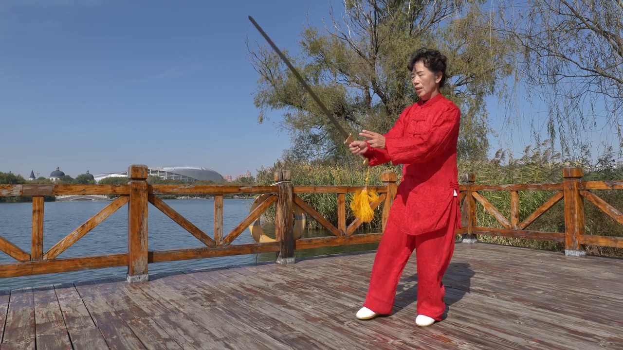一位女士在湖边练太极剑。