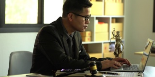 一位男律师在一个木制桌子上放着黄铜天平女神的办公室里工作。司法锤与笔记本电脑法律概念和法律服务
