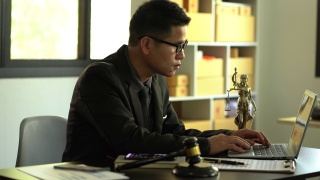 一位男律师在一个木制桌子上放着黄铜天平女神的办公室里工作。司法锤与笔记本电脑法律概念和法律服务视频素材模板下载