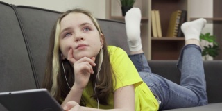 一个快乐的千禧一代白人少女躺在舒适的沙发上听着平板电脑上的音乐
