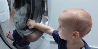 小婴儿，蹒跚学步的孩子看着在洗衣机里洗衣服