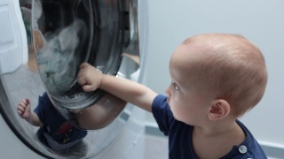 小婴儿，蹒跚学步的孩子看着在洗衣机里洗衣服