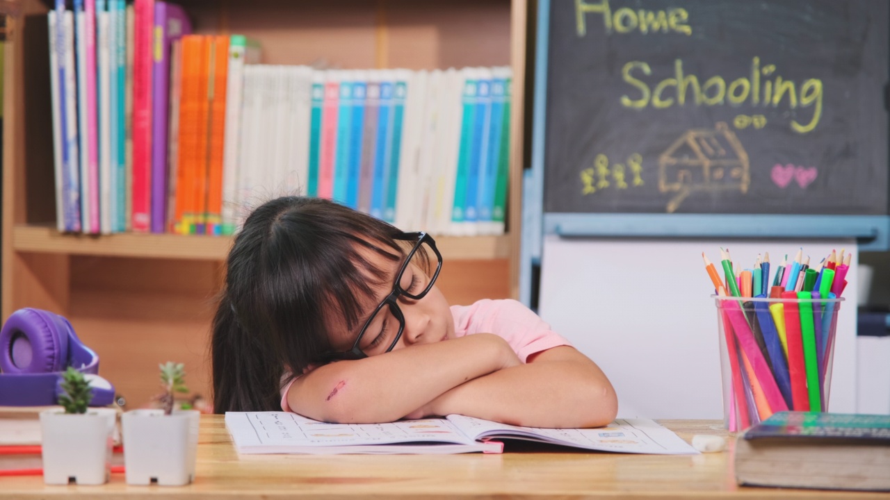 可爱的小女孩做完作业后在桌子上睡觉。新常态家庭教育。