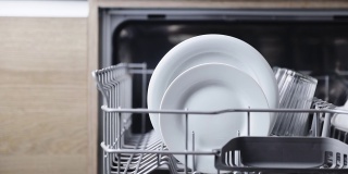 一只妇女的手从开着的洗碗机的篮子里取出洗过的盘子