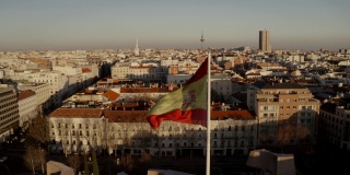 马德里,西班牙。日落时的城市全景、建筑物、街道和屋顶的房屋，从顶部观看。在画框的中央，西班牙国旗迎风飘扬