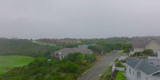 在被树木和灌木包围的大型豪华住宅上空飞行。雾蒙蒙的一天在遥远的市区。南非伊丽莎白港