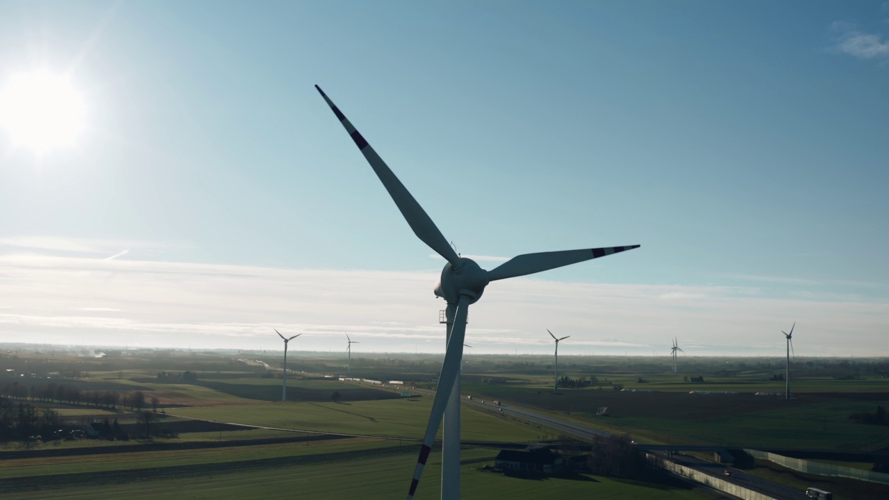 在阳光明媚的秋日，无人机看到风力涡轮机在绿色的农田里通过公路产生清洁的生态电力。风力发电场生产替代绿色可再生能源