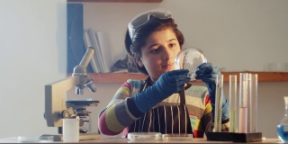 一个十几岁的研究人员在一个家庭实验室里对着实验室设备的背景，在培养皿中检查一株植物。