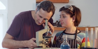 一位父亲帮助他的儿子十几岁在研究家庭实验室通过显微镜对实验室设备的背景进行检查。